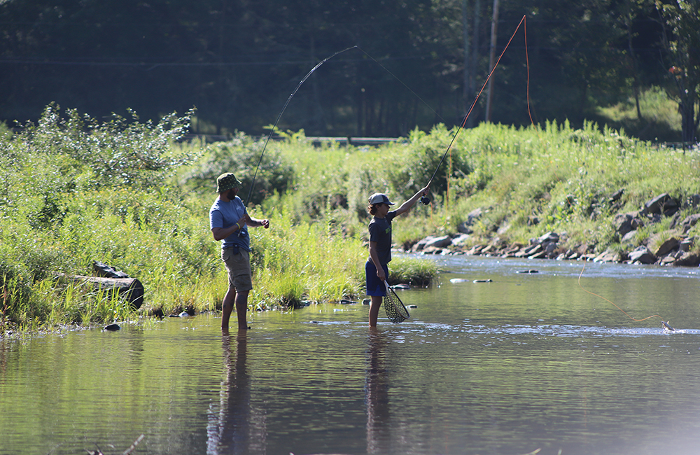 a couple of men standing on top of a river during summer camp activities